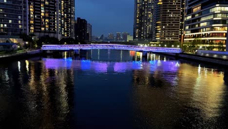 Coloridas-Luces-De-La-Ciudad-Que-Se-Reflejan-En-Una-Superficie-De-Aguas-Tranquilas-Por-La-Noche