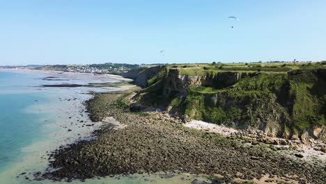 drone footage gliding along the arromanches cliffs, showing their majestic drop into the blue sea, framed by lush green fields under a cloudless sky