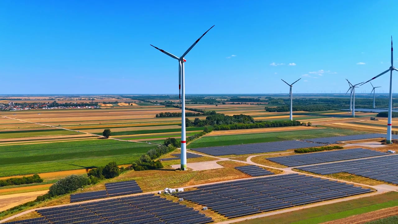 Wind turbines standing in agricultural summer field. Tall white energy generators in open country field. Aerial view, blue clear sky.