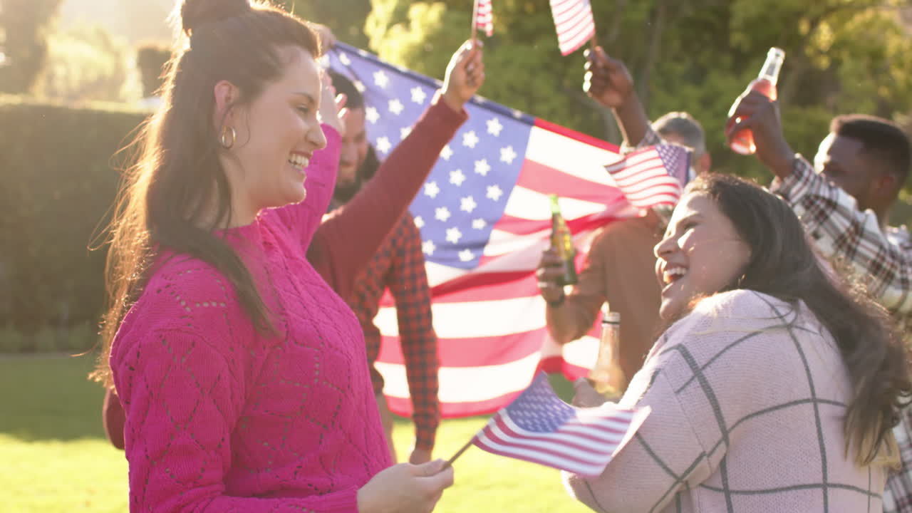 Happy diverse male and female friends dancing with flags in sunny garden