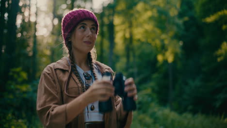 woman wearing knit hat looking through binocular in forest