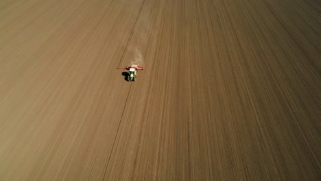 aerial view of a green tractor seeding, sowing agricultural crops at the field with dust behind