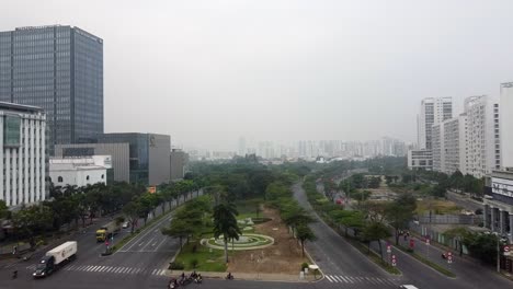 Drone-dolly-above-vietnam-road-intersection-and-park-median-foggy-day