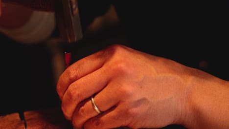 close-up of hands gripping a red pencil over a wooden table, focusing on the fingers and pencil tip.