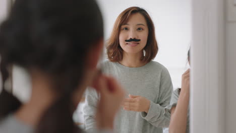 asian mother and daughter playing dress up game at home wearing moustaches little girl having fun with mom enjoying playful day with child together on weekend happy family 4k footage