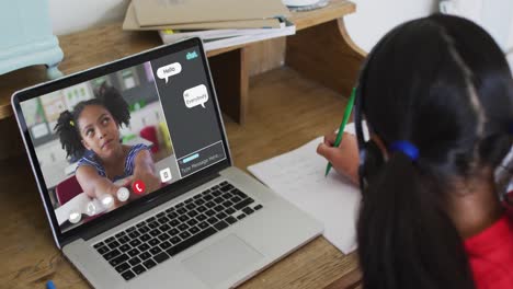 Schoolgirl-using-laptop-for-online-lesson-at-home,-with-girl-talking-and-web-chat-on-screen