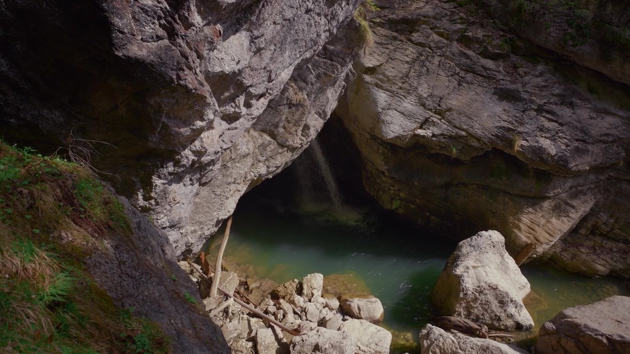 Cascata che scorre da una grotta buia in una pozza limpida. Illuminazione drammatica nella gola di Starzlachklamm.