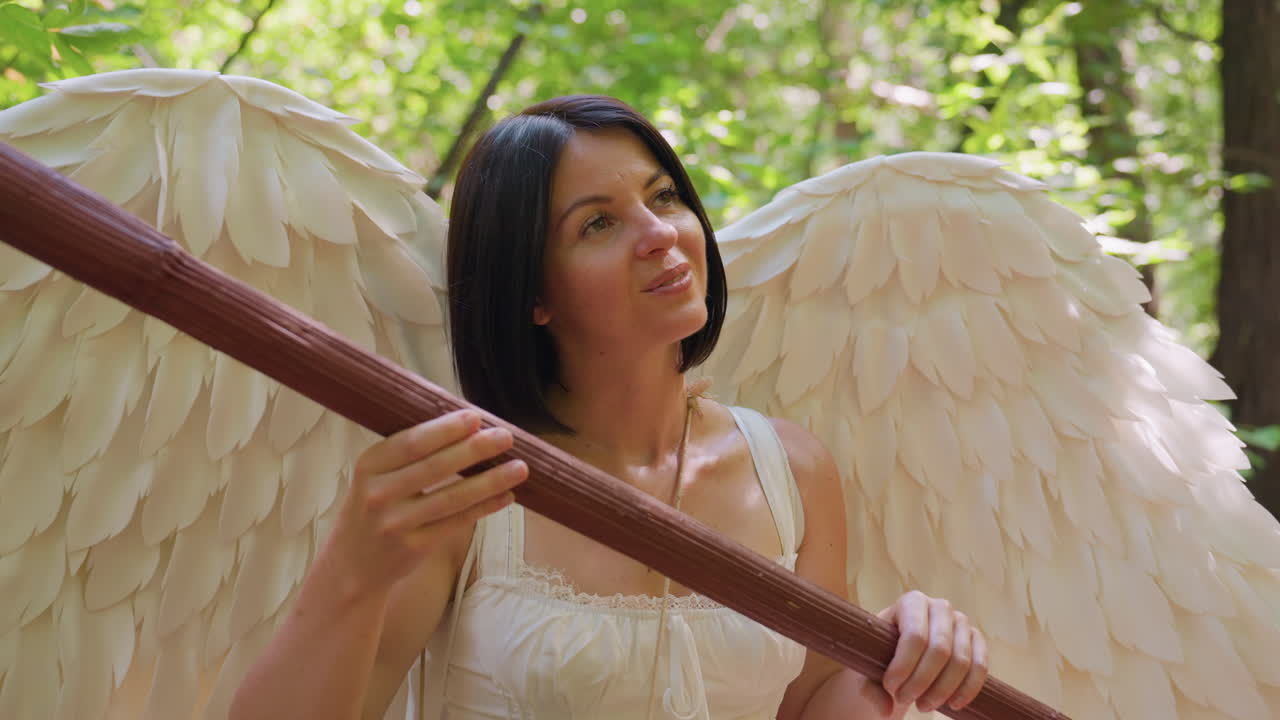 Close up goddess of love seated in forest holding wooden staff, tapping it gently like harp with drum around neck, surrounded by sunlight and green leaves, expressing serenity