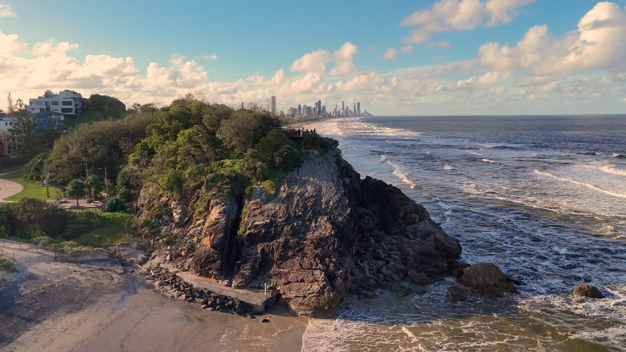 Aerial footage captures coastal erosion at Burleigh Heads, Gold Coast, with waves crashing against rocky cliffs under a clear sky