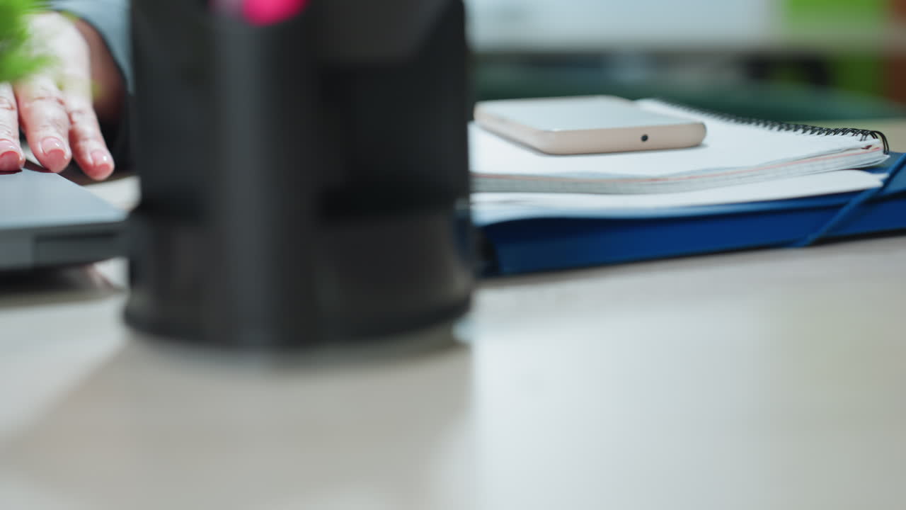 Close up of professional dropping folder on office desk with smartphone and documents placed beside open laptop, capturing workplace setup and start of workday preparation in modern setting