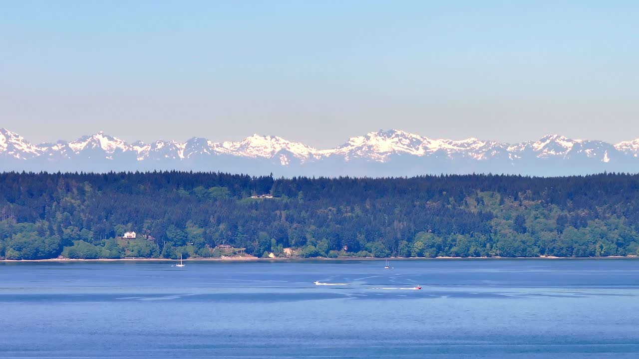 Panoramic View of a Serene Bay with Forested Shoreline and Snow-Capped Mountains