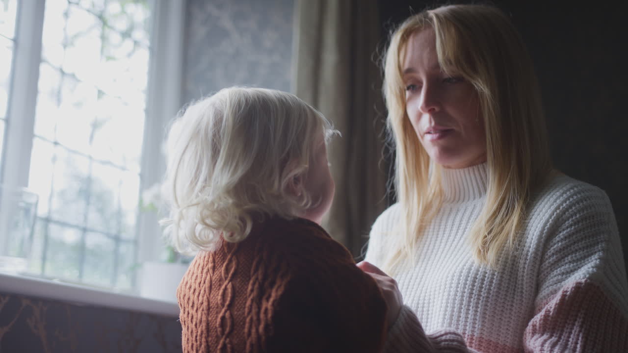 어머니는 아들을 안고 게임을 하고 있습니다. 생활비가 비싼 에너지 위기 중에 집에서 따뜻하게 지내려고 합니다.