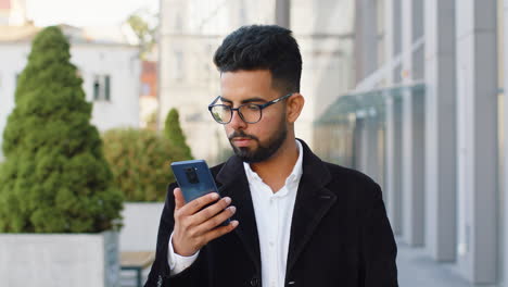 Lächelnder-Geschäftsmann,-Der-Sein-Smartphone-Benutzt-Und-Textnachrichten-Eintippt-Und-Auf-Der-Stadtstraße-Online-Chattet