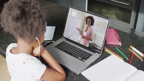 african american girl using laptop for video call, with female teacher on screen