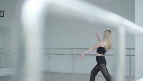 fit girl in black clothes performing contemporary. female dancer shows flowing motions, body and hands waves at white room. modern ballet dance choreography. young woman is moving smoothly