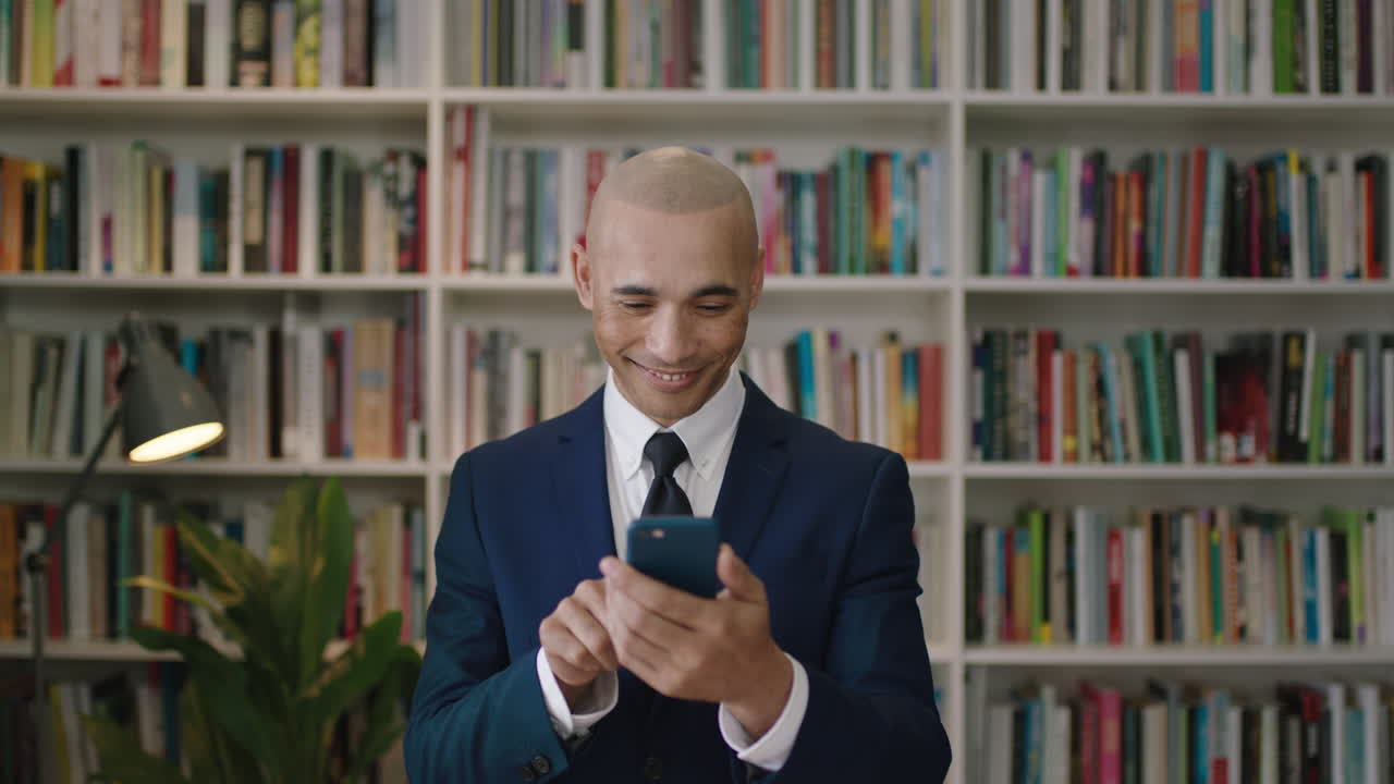 retrato en primer plano de un hombre de negocios hispano calvo que usa un teléfono inteligente sonriendo enviando mensajes de texto a las redes sociales biblioteca de estanterías