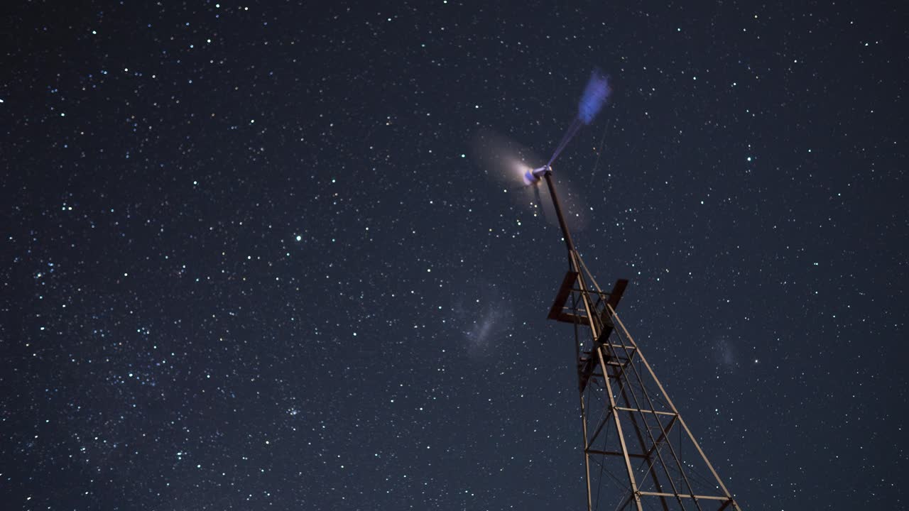 timelapse de una pequeña turbina eólica con estrellas en movimiento en el fondo