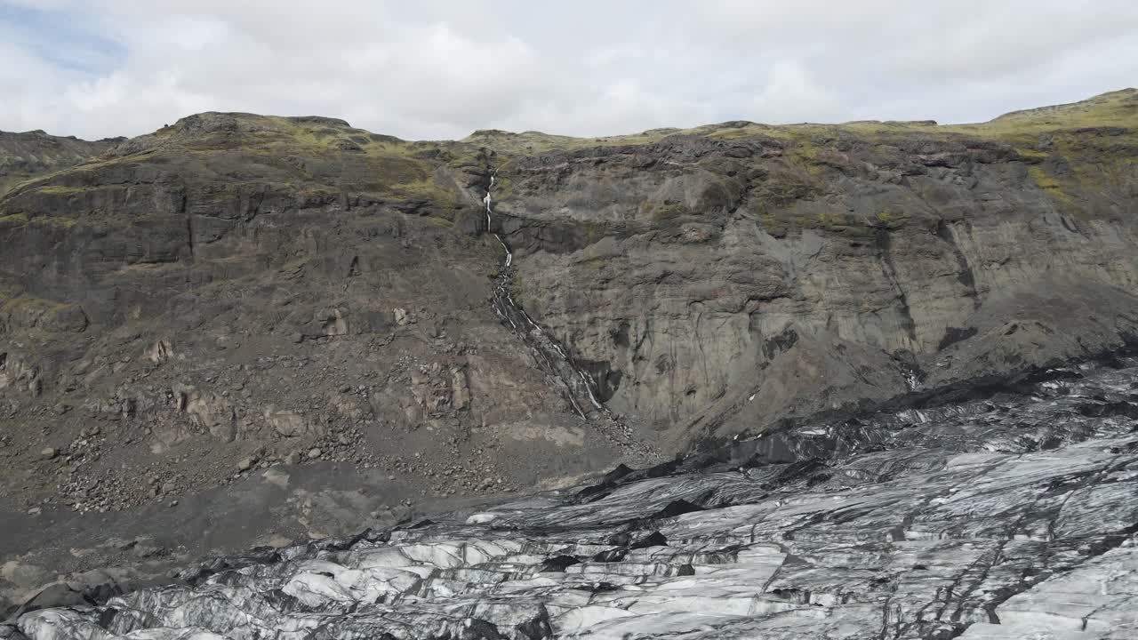 Ascend over Sólheimajökull glacier with an aerial drone, as the camera reveals the vast icy sprawl and towering mountains beyond, showcasing nature's grandeur and icy realm