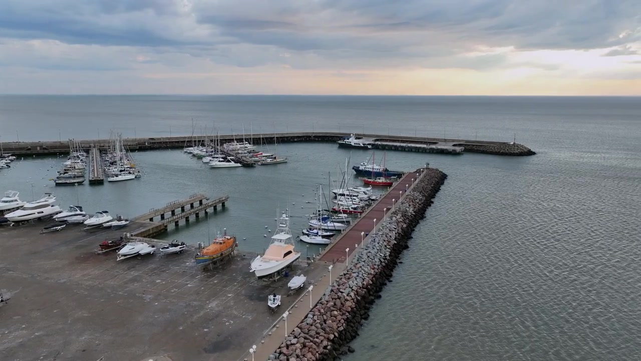 Yacht e frangiflutti nel porto di Piriapolis che mostrano la passerella del molo, barche e yacht ormeggiati e il lungomare costiero dell'Uruguay con vista aerea