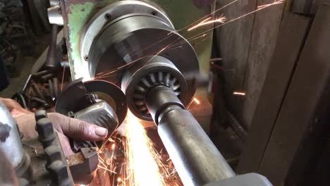 technician is using an electric grinder to grind the work that is being rotated on a lathe.