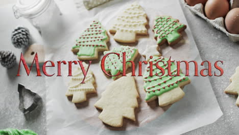 merry christmas text in red over decorated christmas cookies and on kitchen worktop