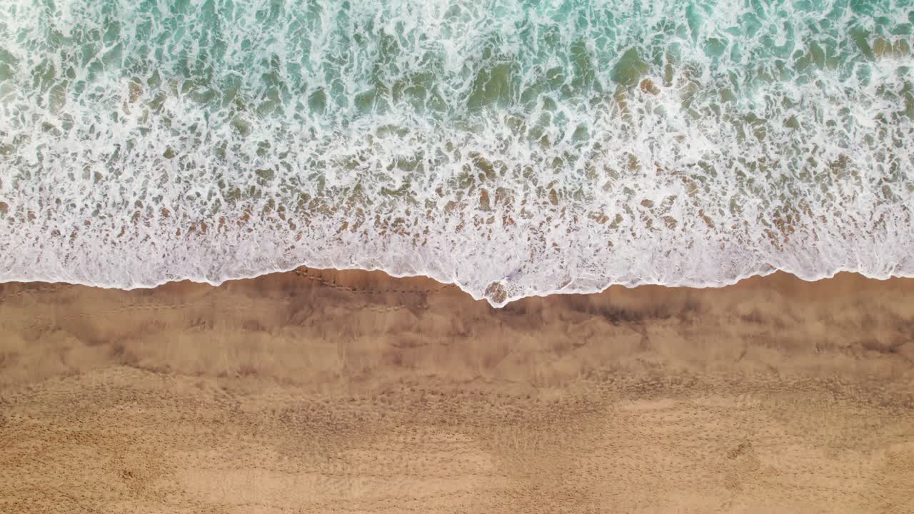 Ascending scenic view of waves crashing on the golden sands with women in white dress at Cofete Beach, Fuerteventura, with vibrant turquoise waters and untouched shoreline by 4k drone