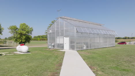 Steady-Camera-Movement-Along-a-Path-Leading-to-a-Glass-Greenhouse-Surrounded-by-Open-Countryside-Fields