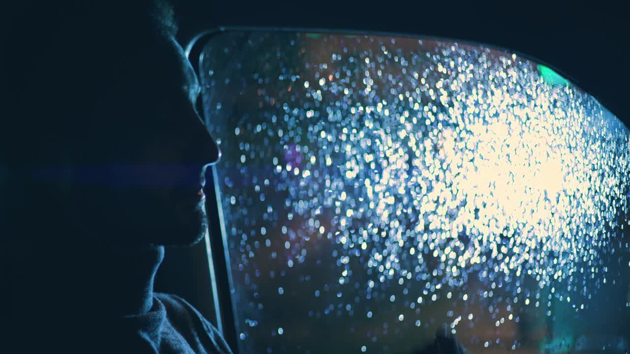 젊은 잘생긴 남자가 비가 오는 밤에 차에 앉아 있습니다.