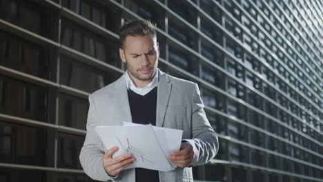 Executive-reading-documents-on-city-street.-Businessman-examining-papers-oEtside