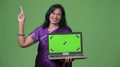 mature happy beautiful indian woman showing laptop and pointing up