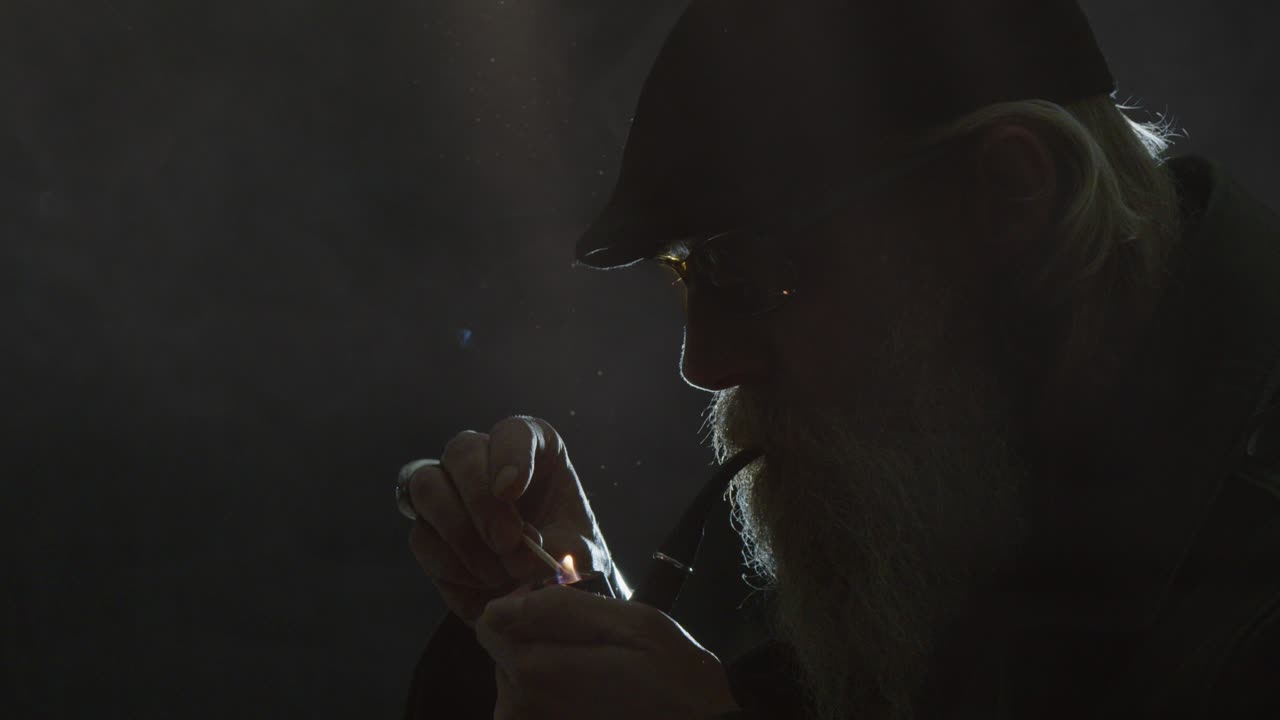 Close up hipster man lights pipe in darkness, creative stage lighting