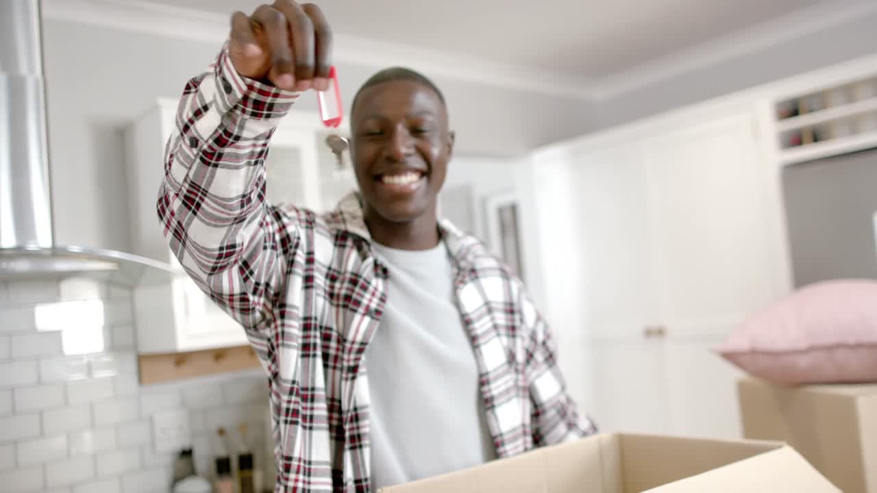 Retrato de homem afro-americano feliz segurando chaves na cozinha em casa, câmera lenta