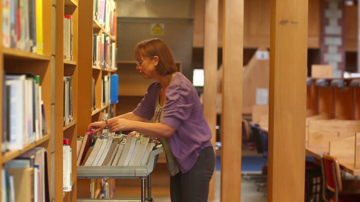 Bibliotecario che spinge un carrello attraverso la biblioteca riponendo i libri