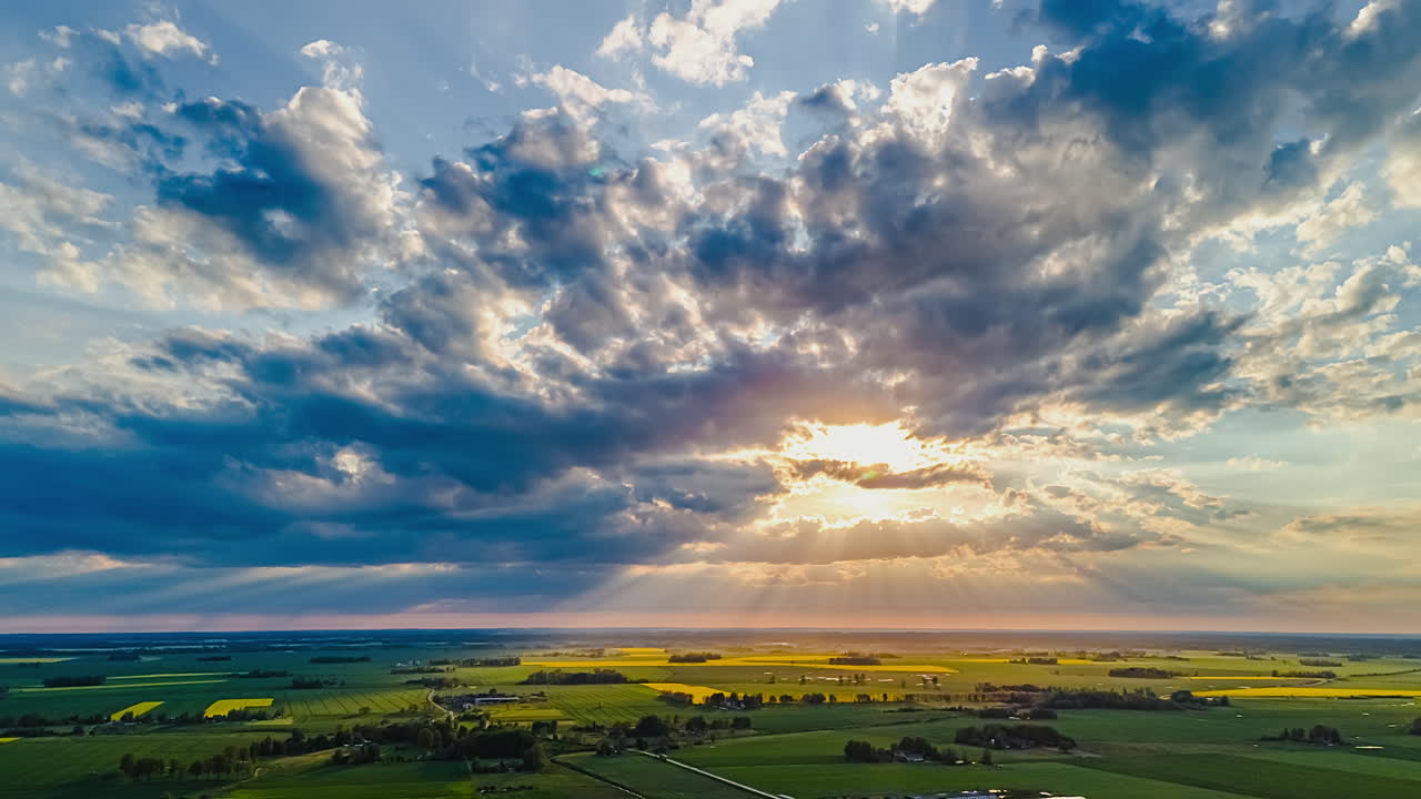Rays of sun shining through clouds over farmland fields in rural Europe in this cloudscape aerial time lapse