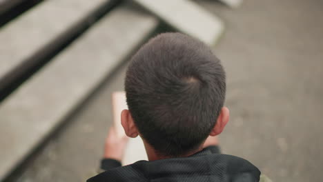 close up aerial overhead view of boy seated outdoors concentrating on study while flipping pages of book with blurred ground and stair background