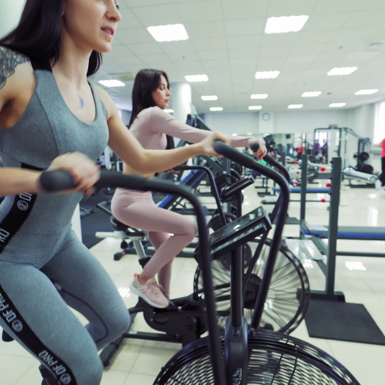 Fit young sexy women in sportswear using indoor bikes at the gym. Strong female athletes are doing cardio workout on cycles at health club.