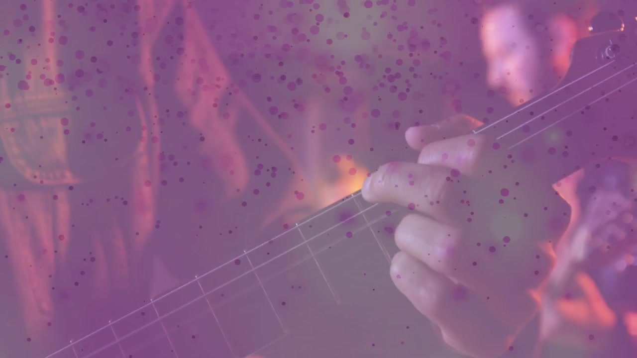 Guitarrista fazendo acordes durante a apresentação enquanto a câmera ajusta o foco e um efeito roxo aparece sobre o braço.