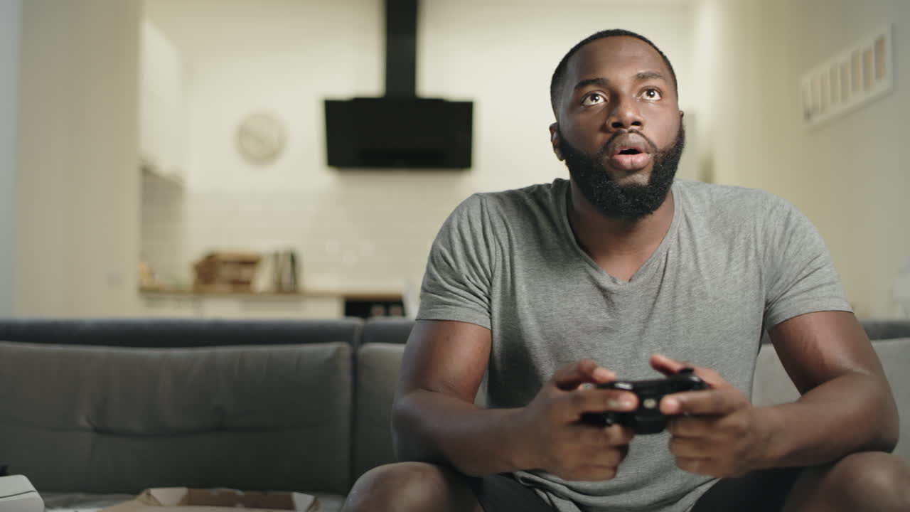 hombre negro sonriente jugando videojuegos en la cocina de su casa.