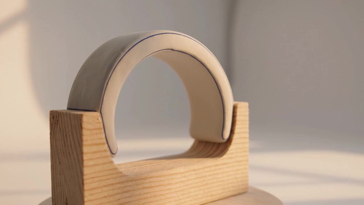 Elegant Ceramic Arch Resting on Wooden Base Showcasing Minimalist Design and Craftsmanship in a Softly Lit Contemporary Setting