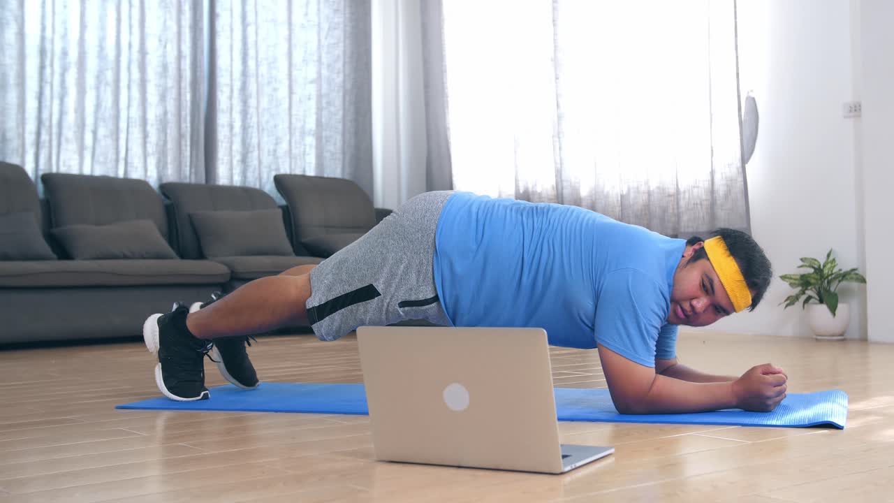 Overweight Man Struggling To Do Plank Exercising At Home While Looking At His Laptop
