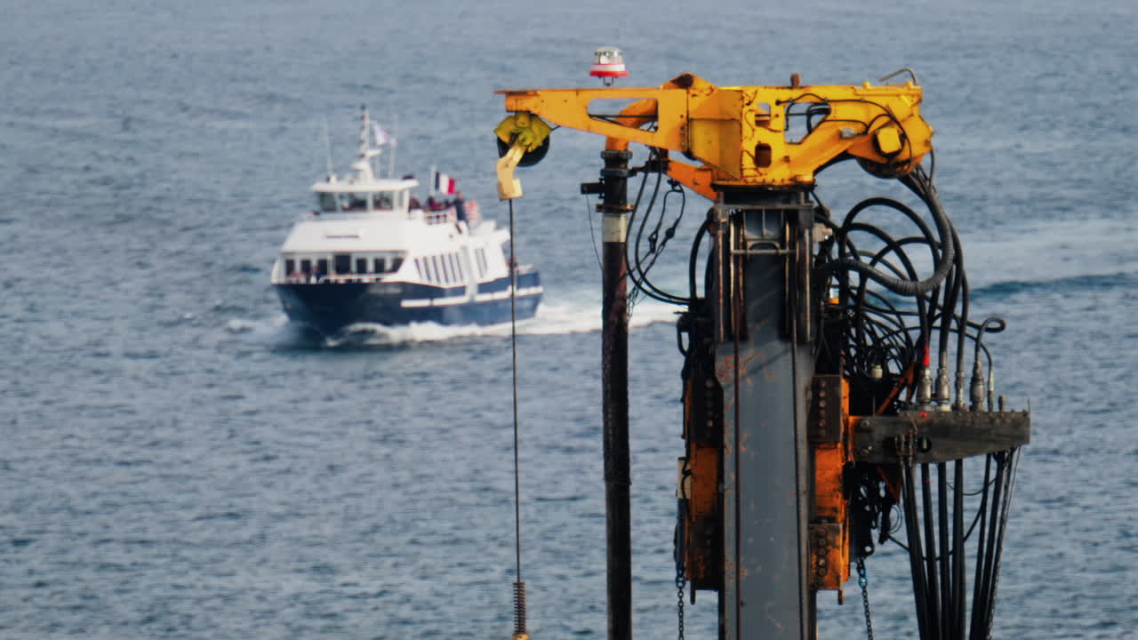 Close up of a yellow crane machine with a boat with the French flag moving on the beach on the background