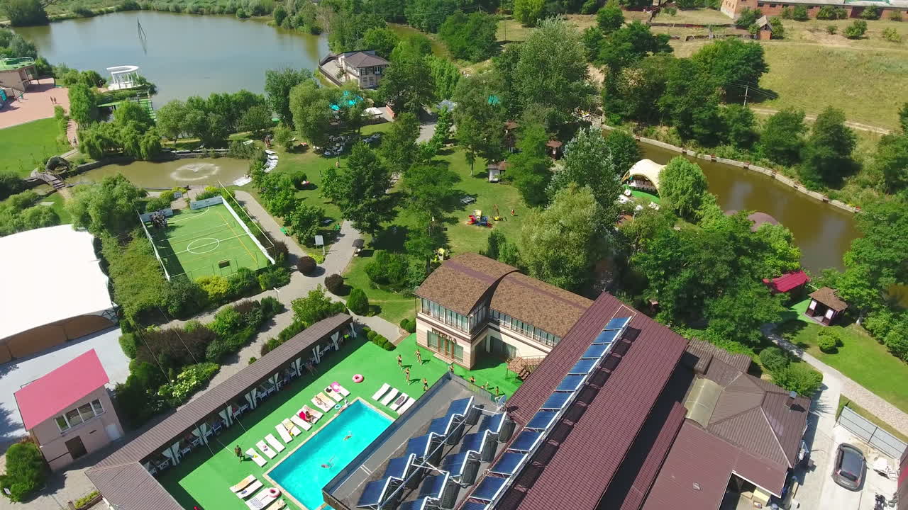 The territory of modern spa resort outside the city. Swimming pool with people resting around and having fun activities. Aerial perspective.
