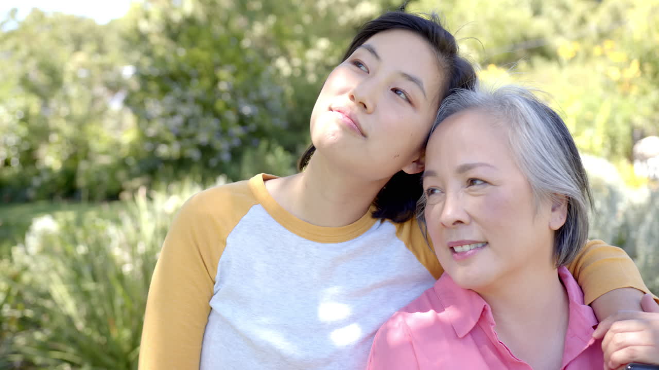 Smiling asian woman embracing elderly asian woman outdoors, enjoying quality time together