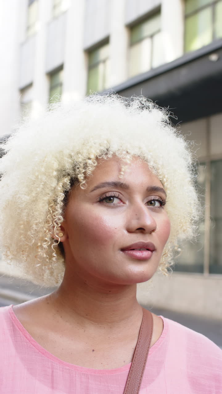 Vertical video: Smiling woman with curly hair standing outdoors, wearing pink top