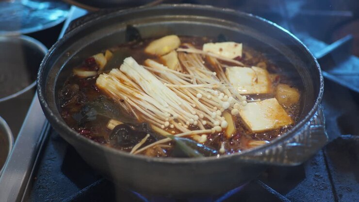 Hot pot che sobbolle con funghi Enoki e tofu su un fornello.