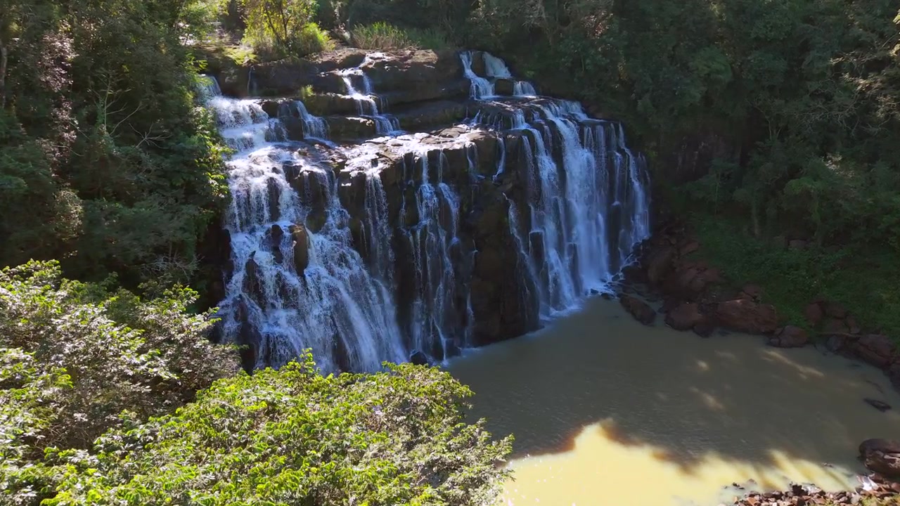 Cachoeira de rio larga e rochosa no meio da exuberante Mata Atlântica verde. Aproximação aérea descendente em câmera lenta em uma tarde ensolarada