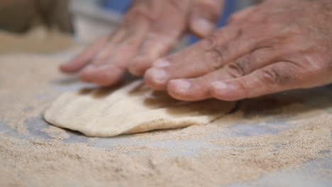 Close-up of hands pressing and shaping dough with flour