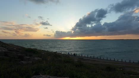 sunset cloudscape over sea, people taking an evening walk, static view