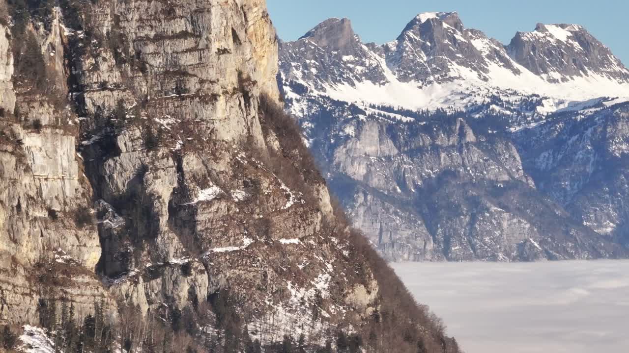 Rocky cliffs and alpine peaks with patches of snow rising above fog in Amden Switzerland
