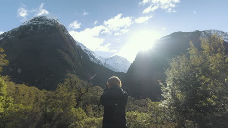 niña fotografiando montañas cubiertas de nieve y exuberantes bosques y valles verdes en un día soleado en nueva zelanda